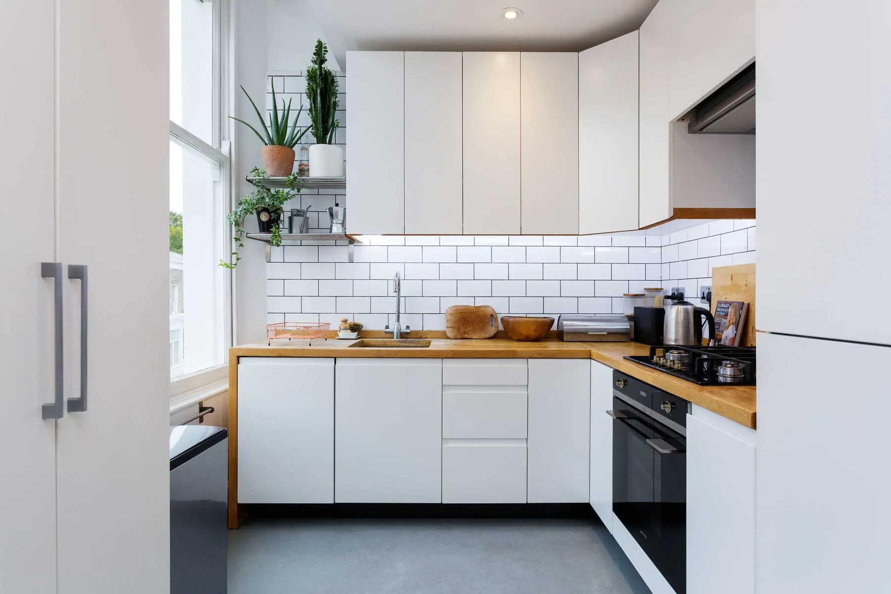 A bright kitchen with white cabinets, tiled walls, and wooden countertops.