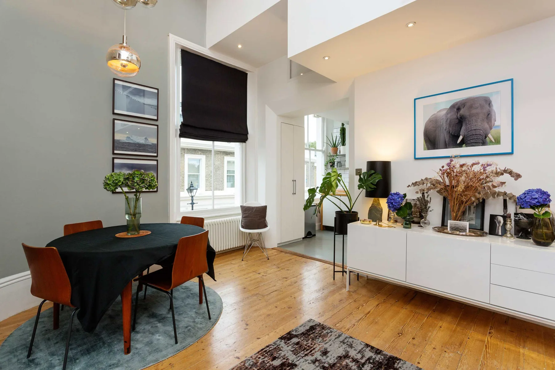 A bright dining and living area with a round table and framed elephant picture.