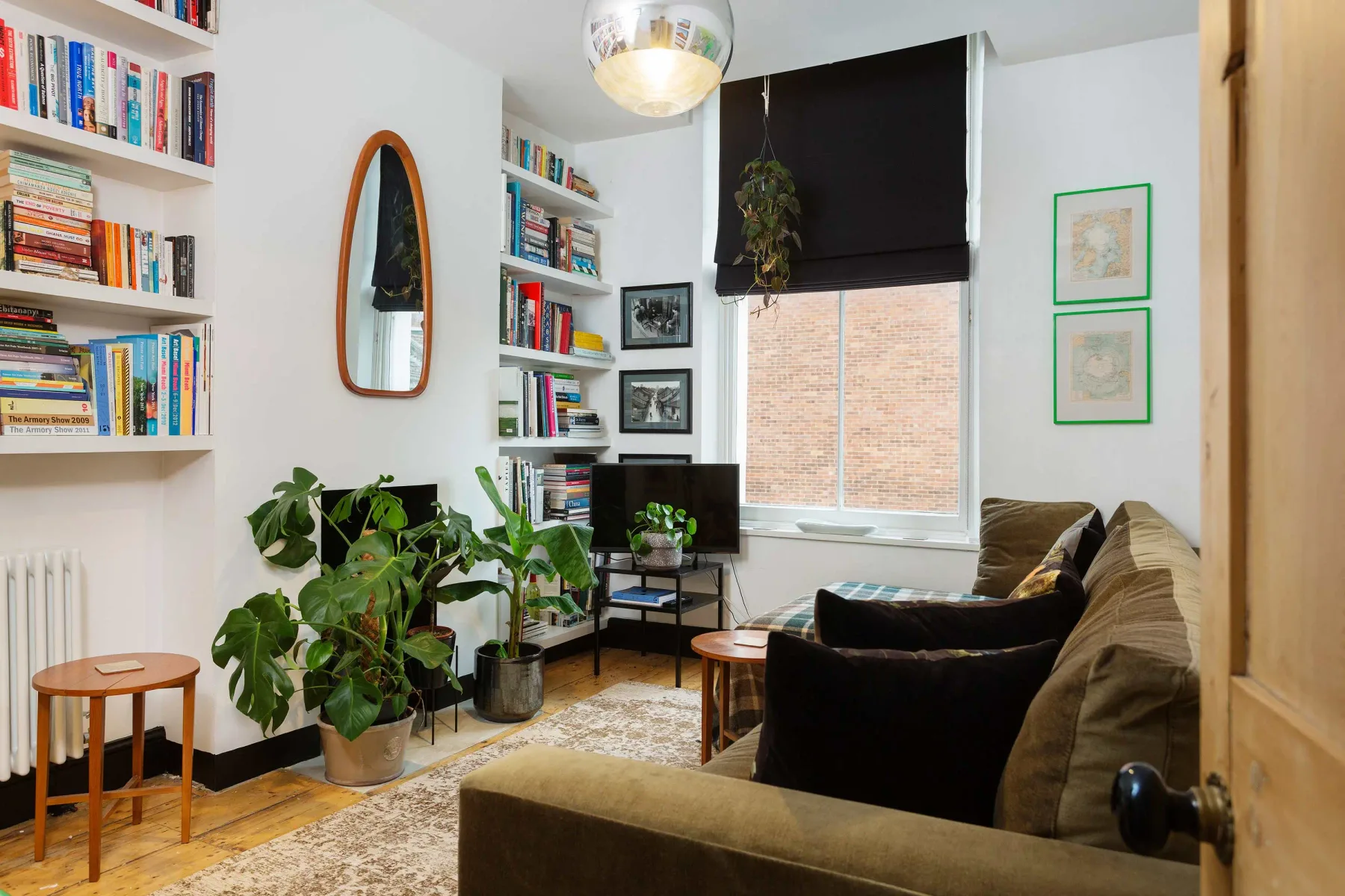 A living room with bookshelves, seating, and plants around a window.