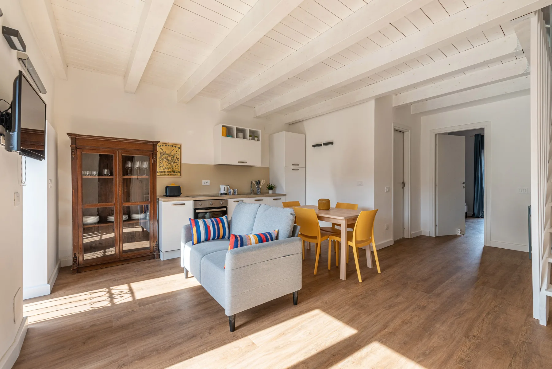 A bright open-plan living and dining area with a compact kitchen and exposed ceiling beams.