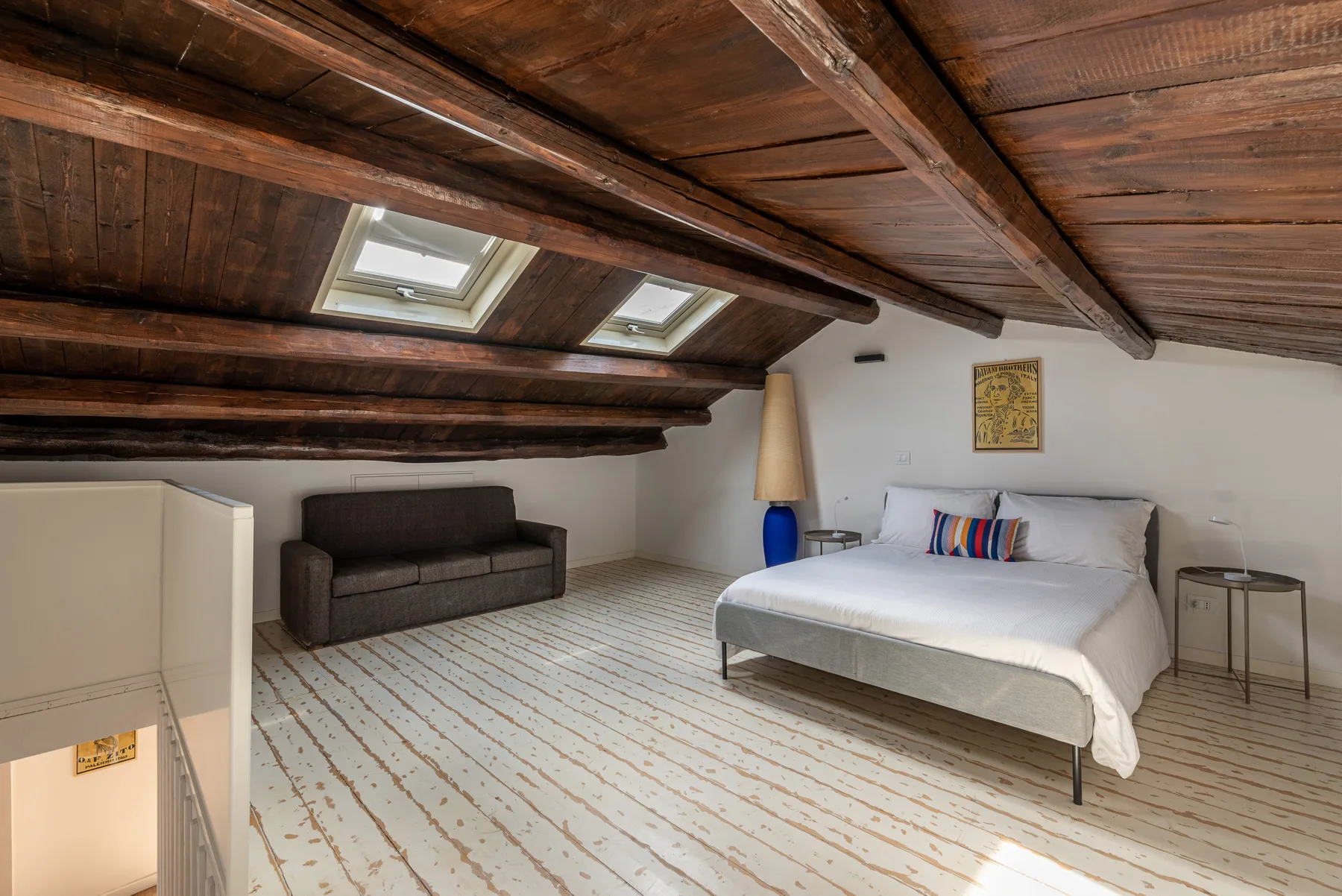 A bedroom with a bed and seating beneath a sloped wooden ceiling.