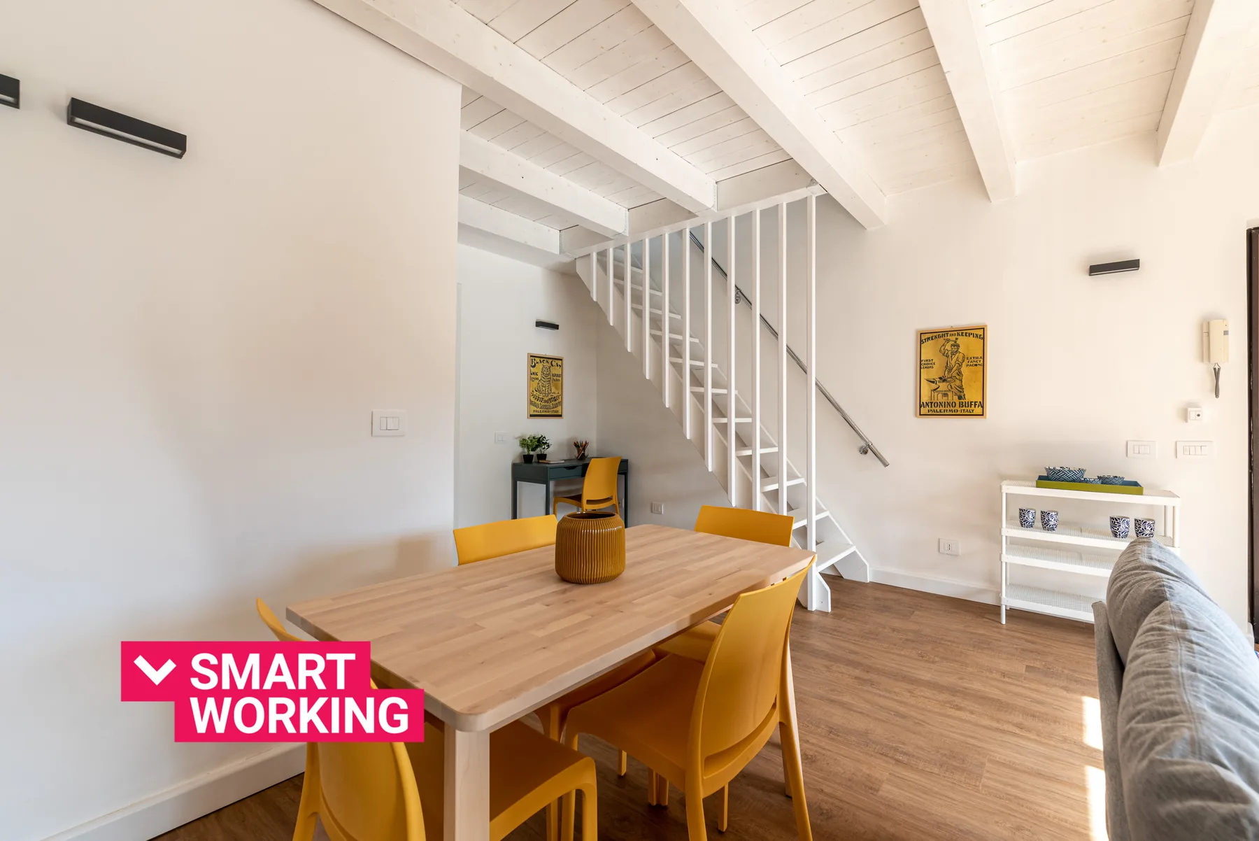 A bright dining area with a wooden table beneath an open staircase.
