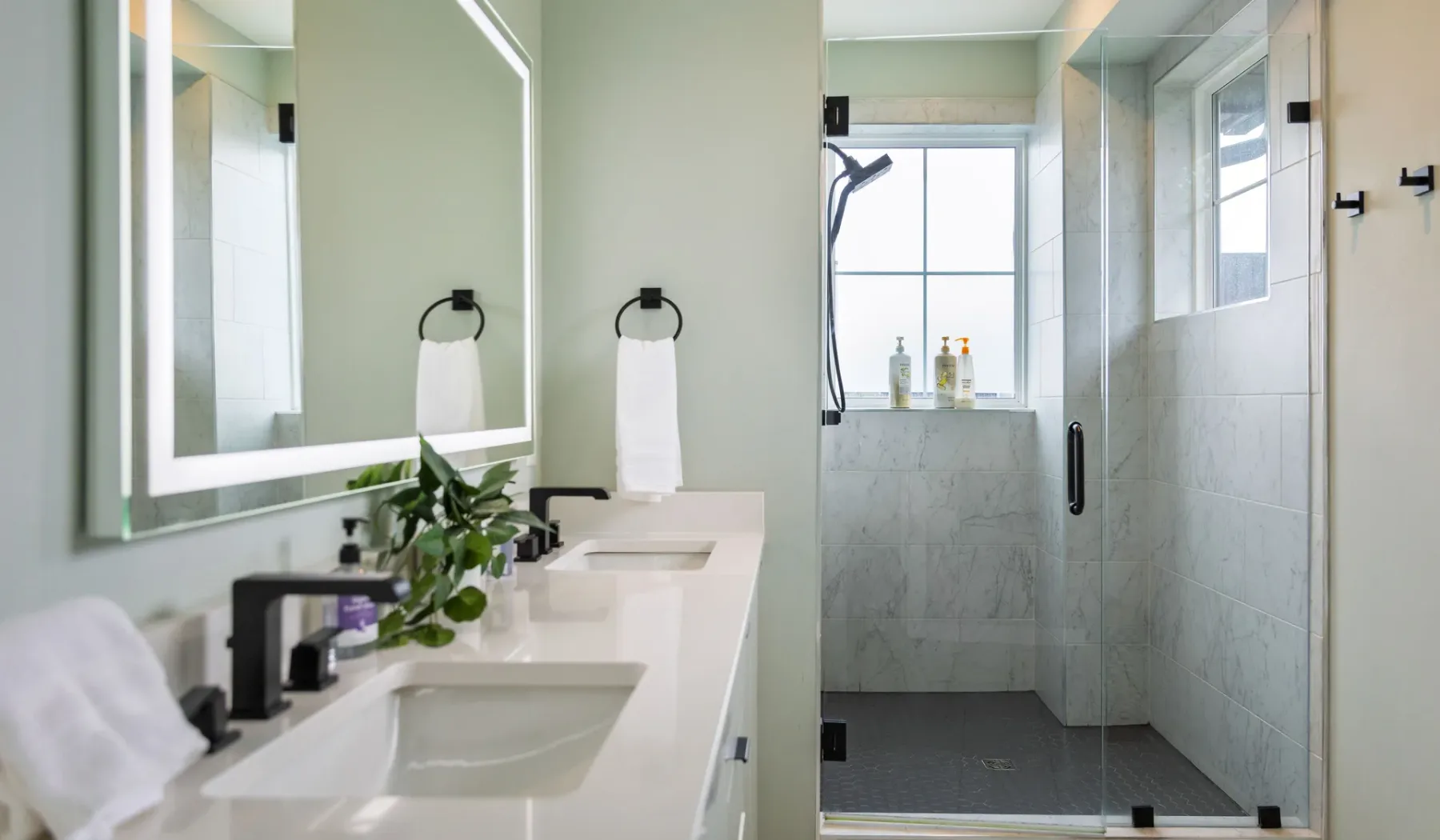 Un baño luminoso con un tocador alargado, espejos y una ducha con mampara de vidrio.