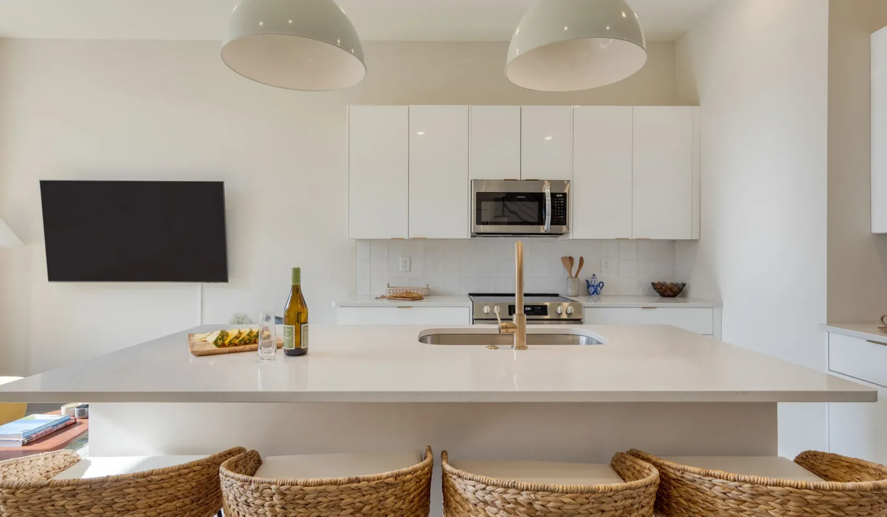 Una cocina luminosa con una isla amplia, asientos de bar y un televisor en la pared.