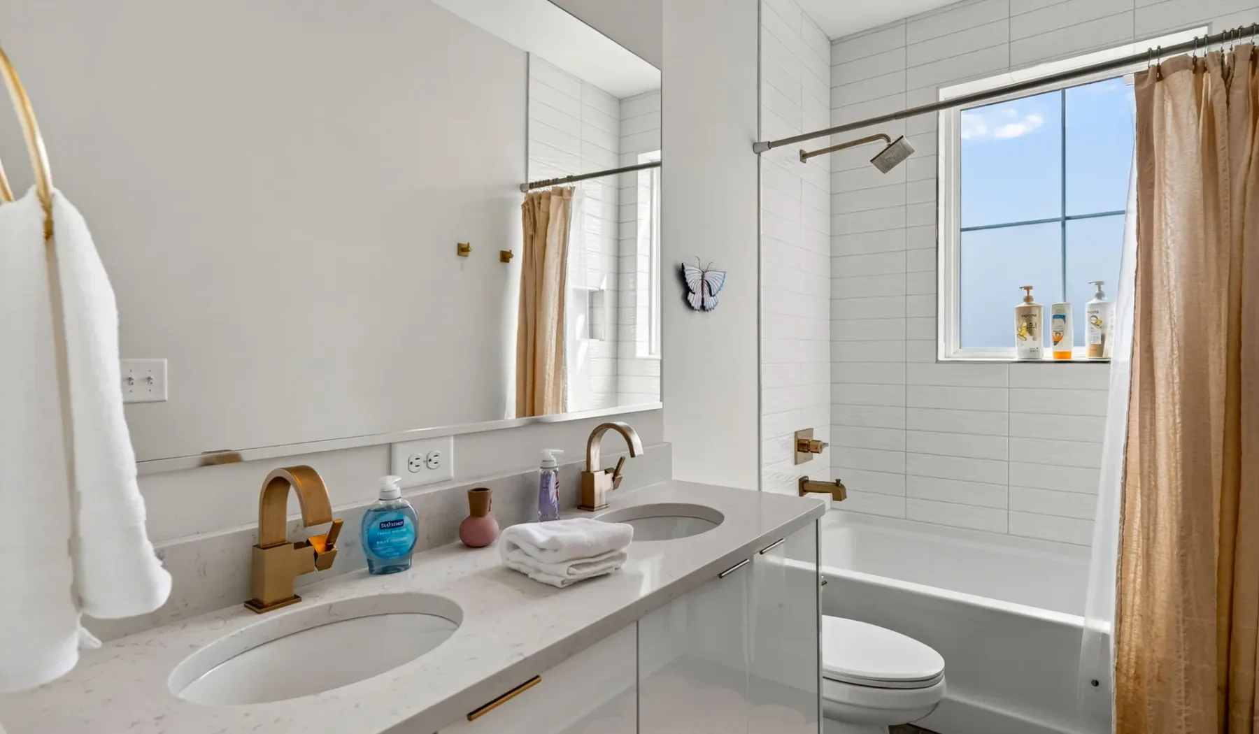 Un baño luminoso con lavabo doble, bañera y ventana.