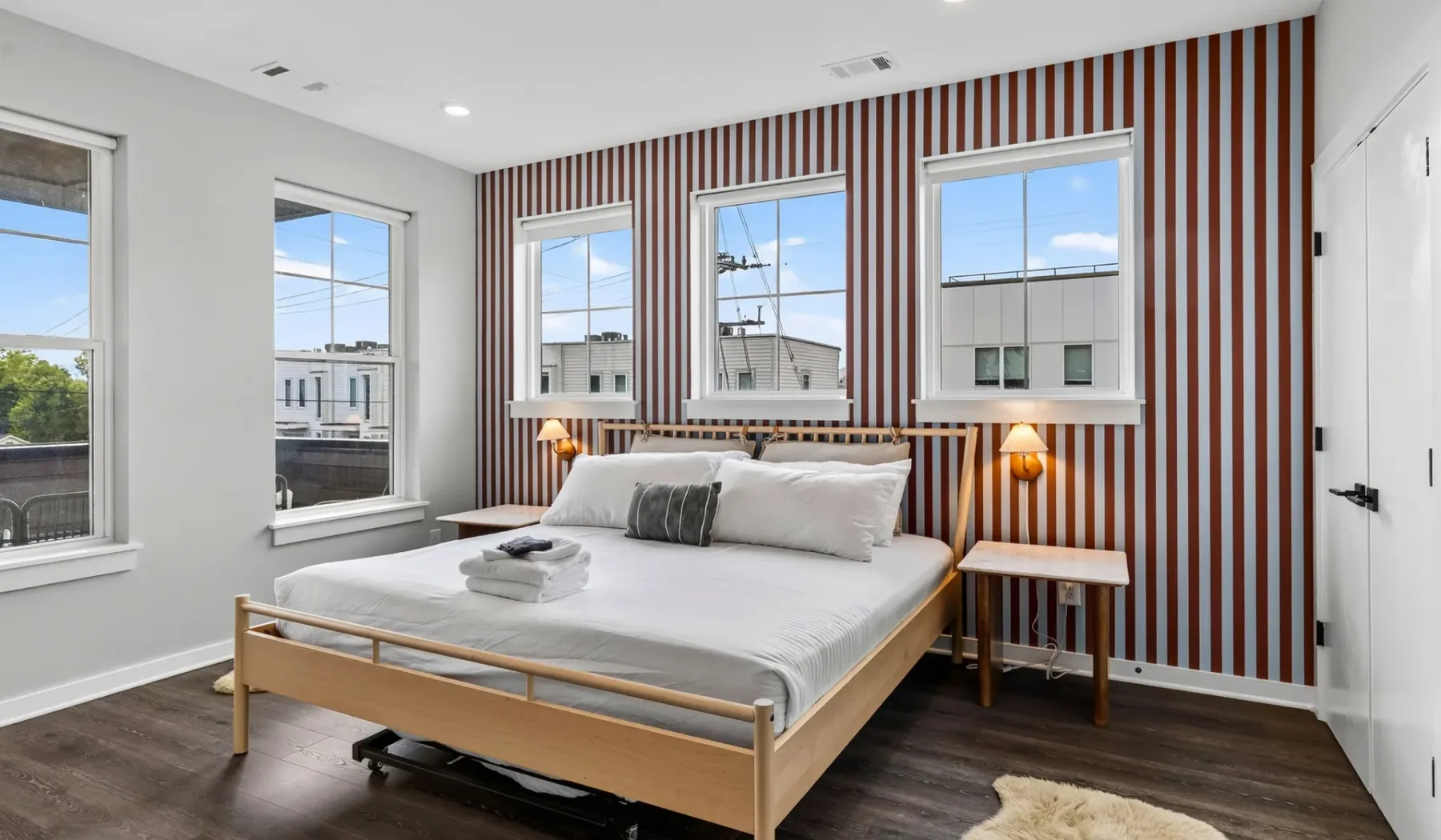 Un dormitorio con una cama frente a una pared decorativa a rayas y ventanas.
