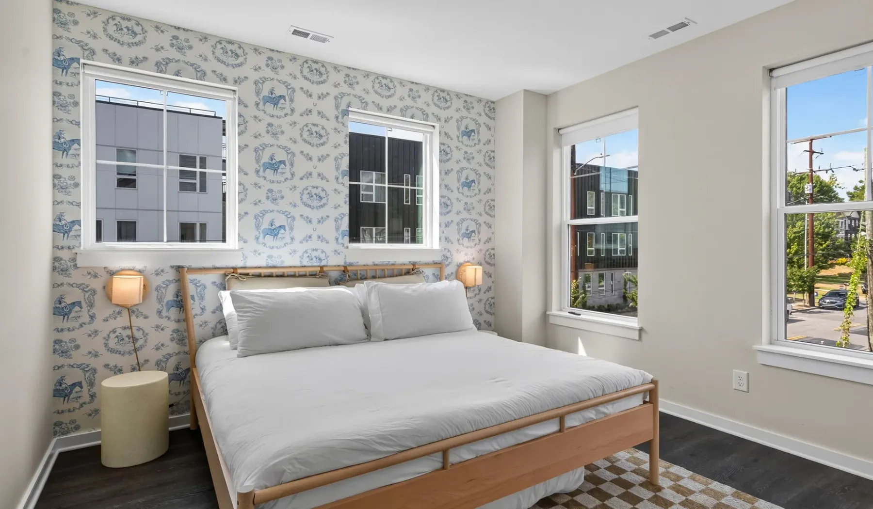 Un dormitorio con una cama, papel tapiz estampado y ventanas grandes.