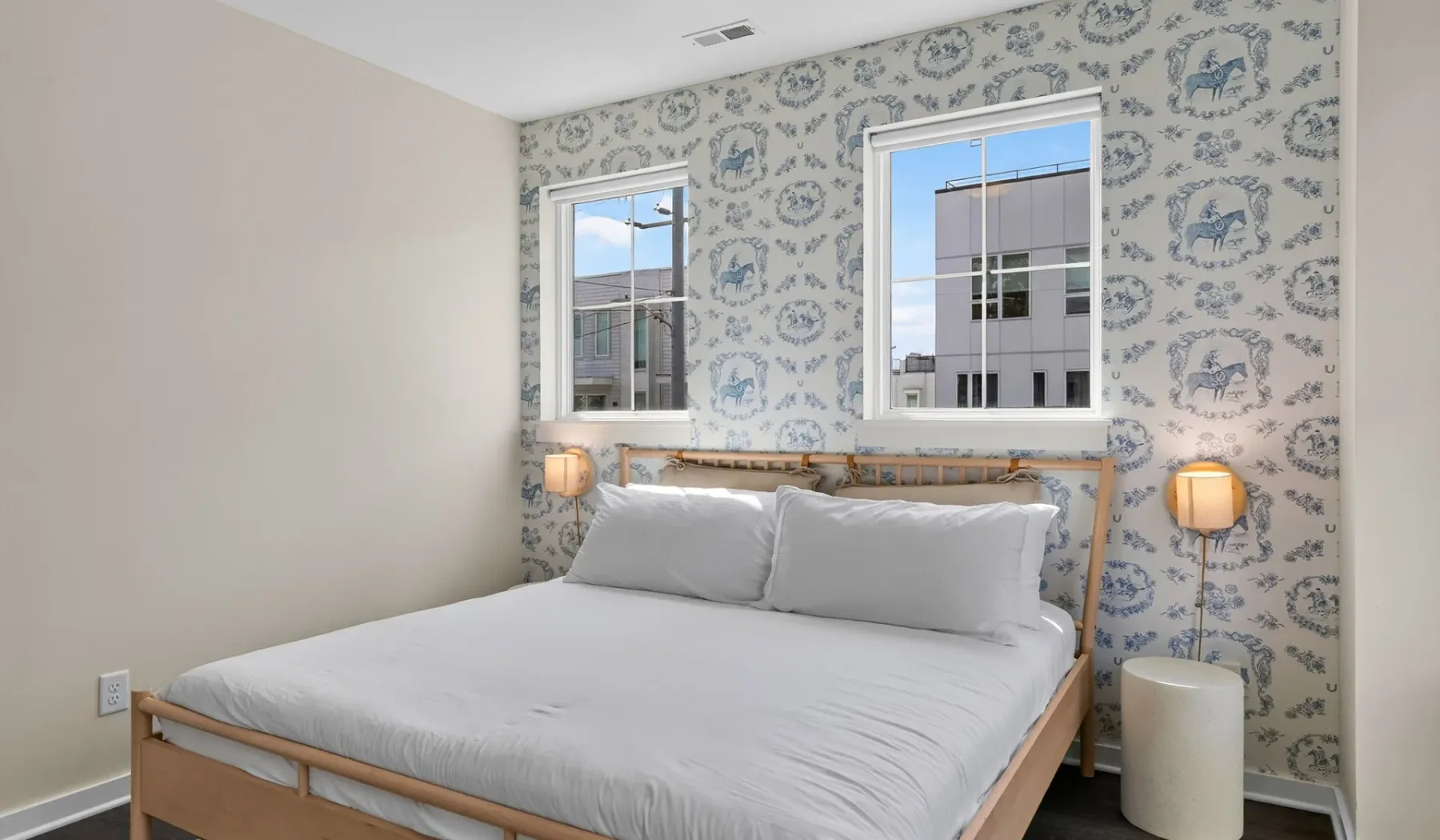 Un dormitorio con una cama, papel tapiz estampado y dos ventanas.