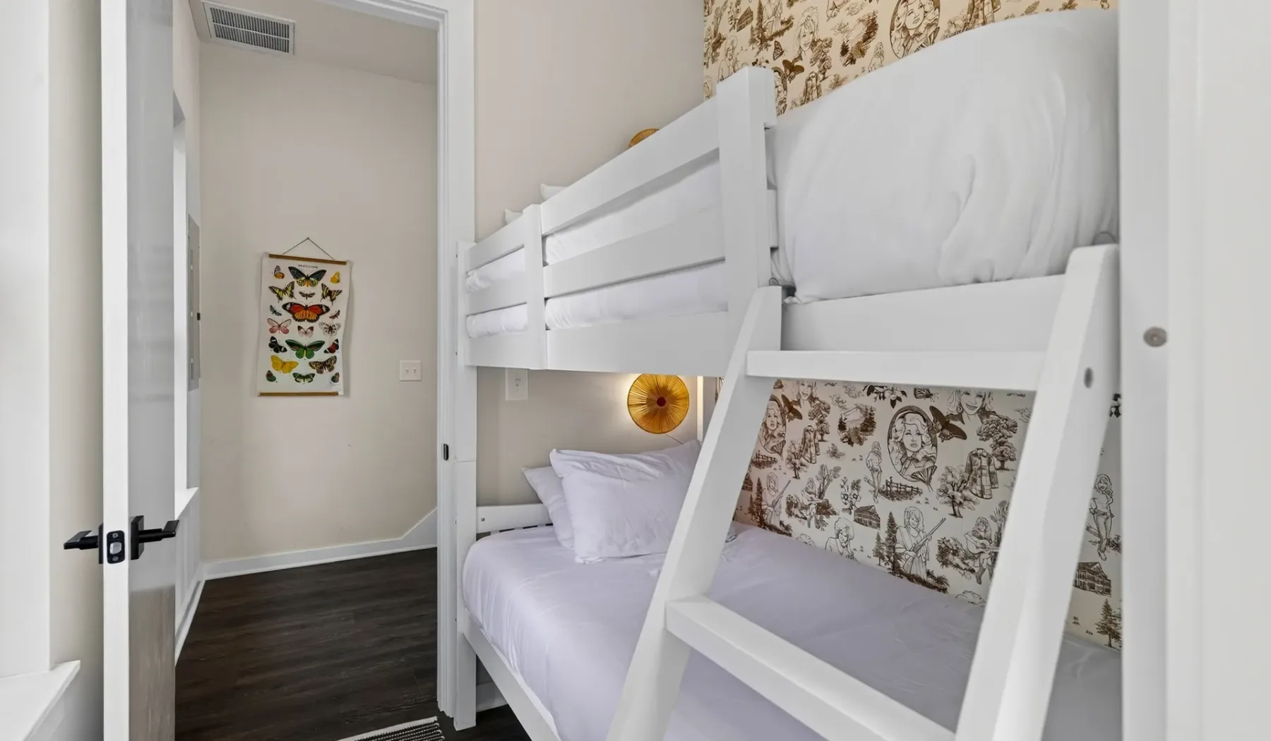 Una litera con ropa de cama blanca está junto a una pared estampada en un dormitorio pequeño.