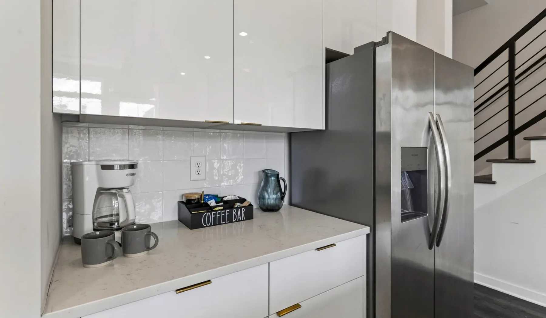 Una encimera de cocina moderna con una cafetera junto a un refrigerador de acero inoxidable.