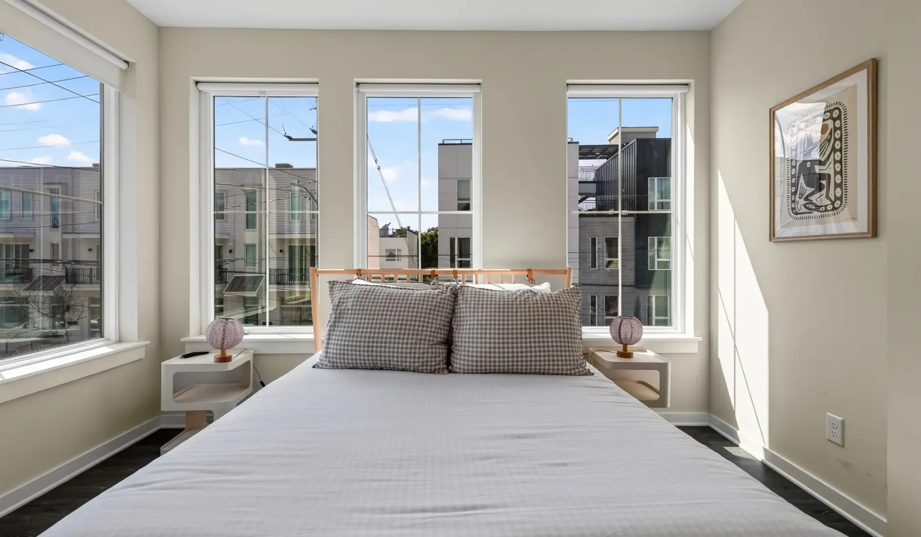 Un dormitorio luminoso con una cama entre ventanas altas.