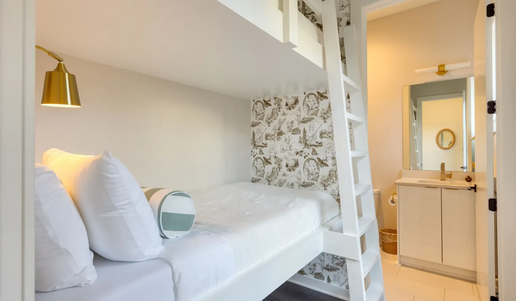 Un dormitorio compacto con una cama elevada junto a una pared estampada y un baño abierto.