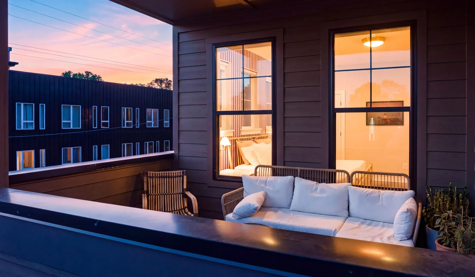 Una zona de estar en un balcón con sofá y vistas a edificios vecinos al atardecer.