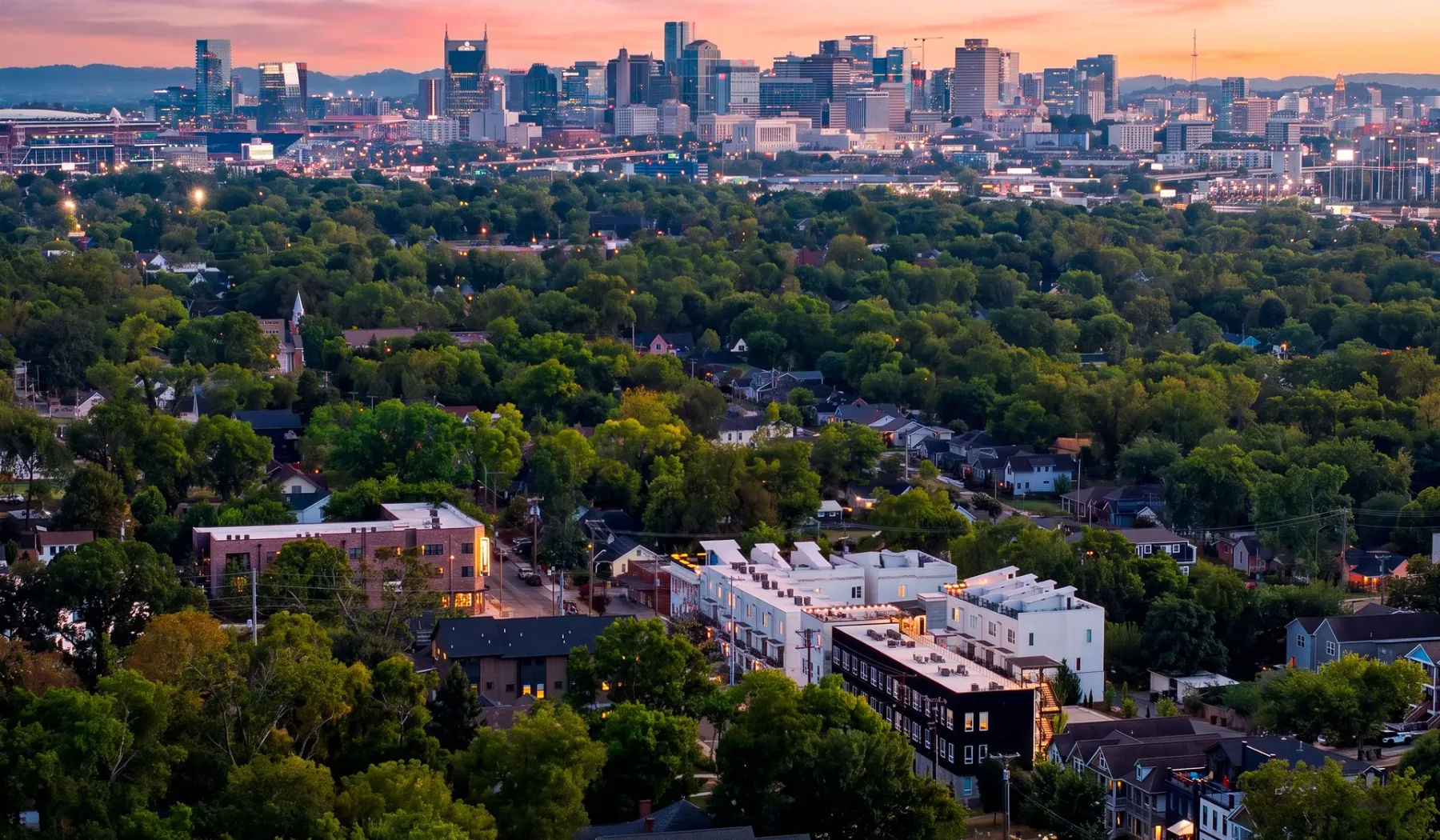 El horizonte de la ciudad se alza tras un extenso barrio residencial arbolado al atardecer.
