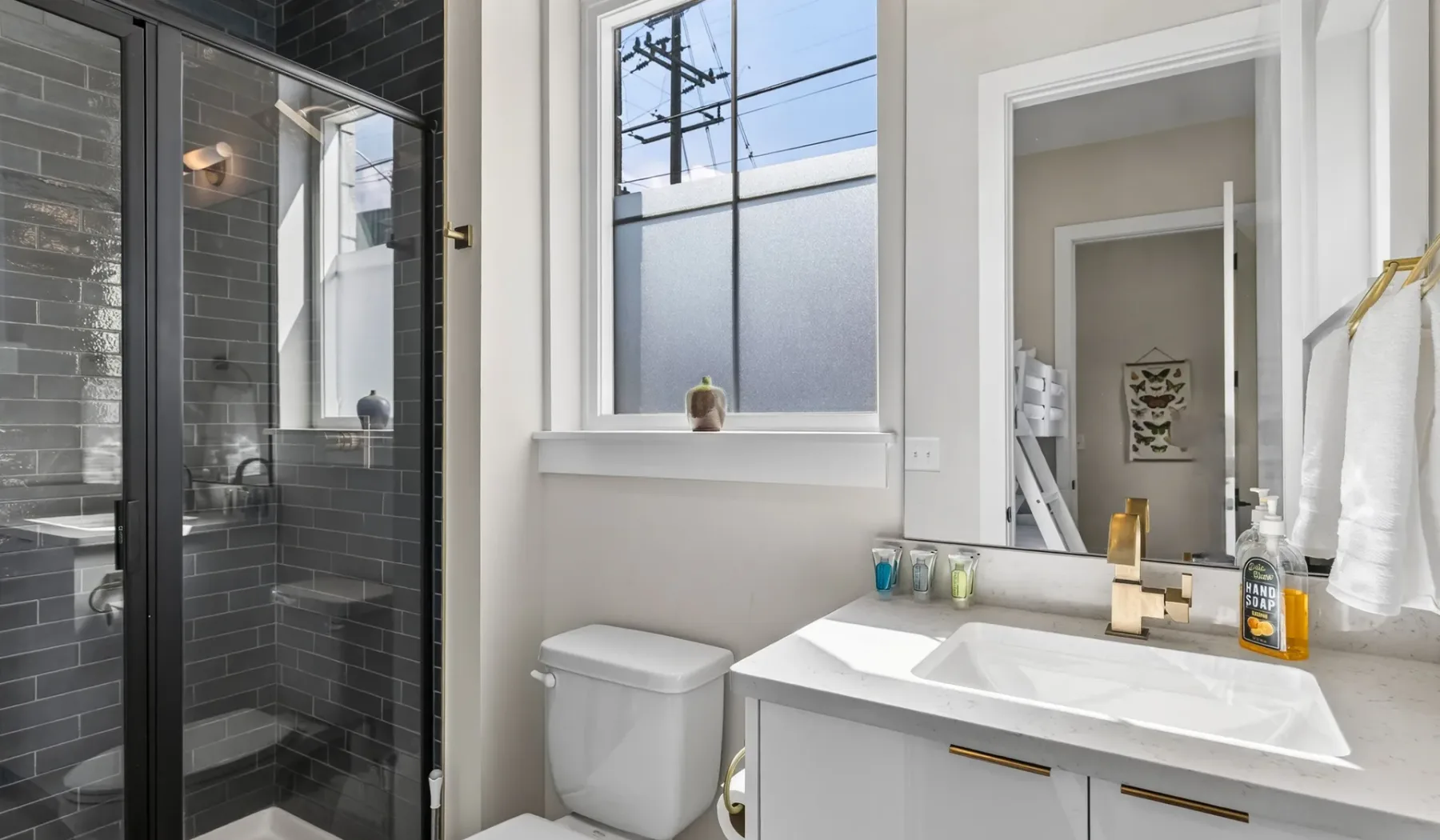 Un baño con ducha de vidrio, mueble de lavabo blanco y una ventana amplia.