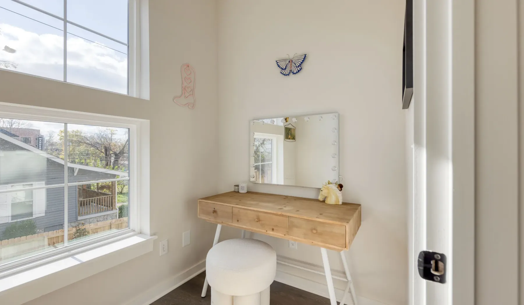 Un área de tocador luminosa con espejo de pared, taburete y ventanas grandes.