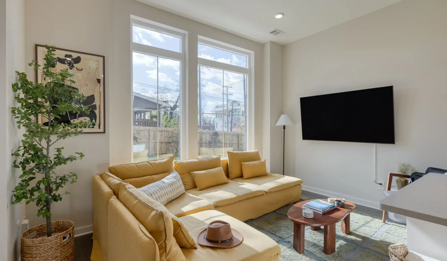 Una sala luminosa con asientos amarillos, un televisor en la pared y ventanales.