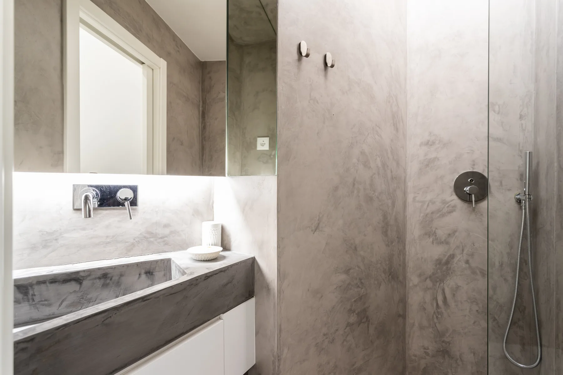 Un baño con lavabo, espejo y accesorios de ducha montados en la pared.