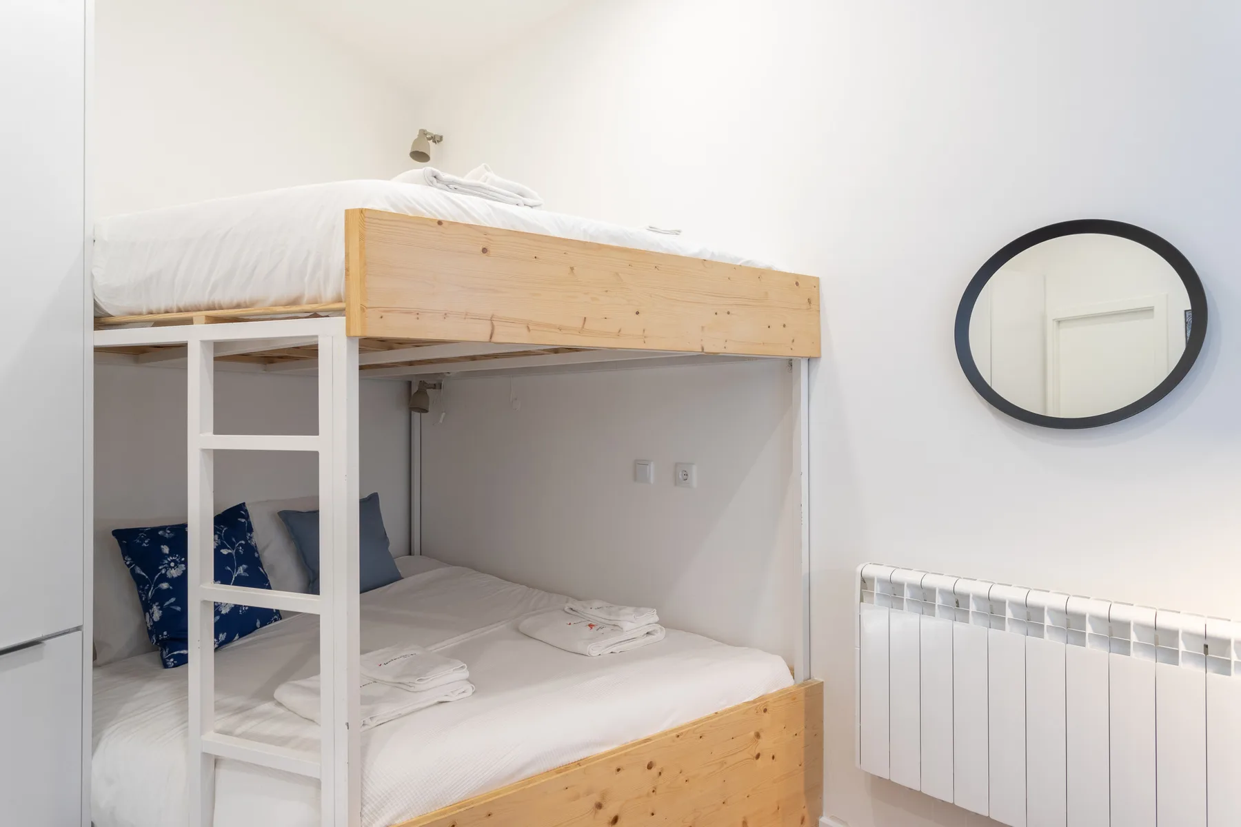 Dormitorio con una litera de madera y un espejo redondo en la pared.