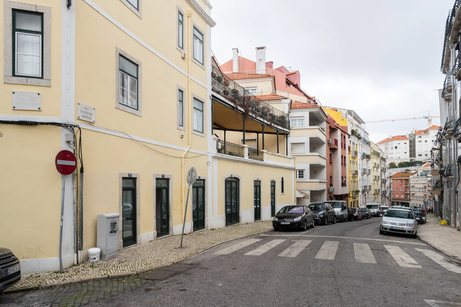 Una calle estrecha bordeada de edificios de tonos pastel y coches aparcados.