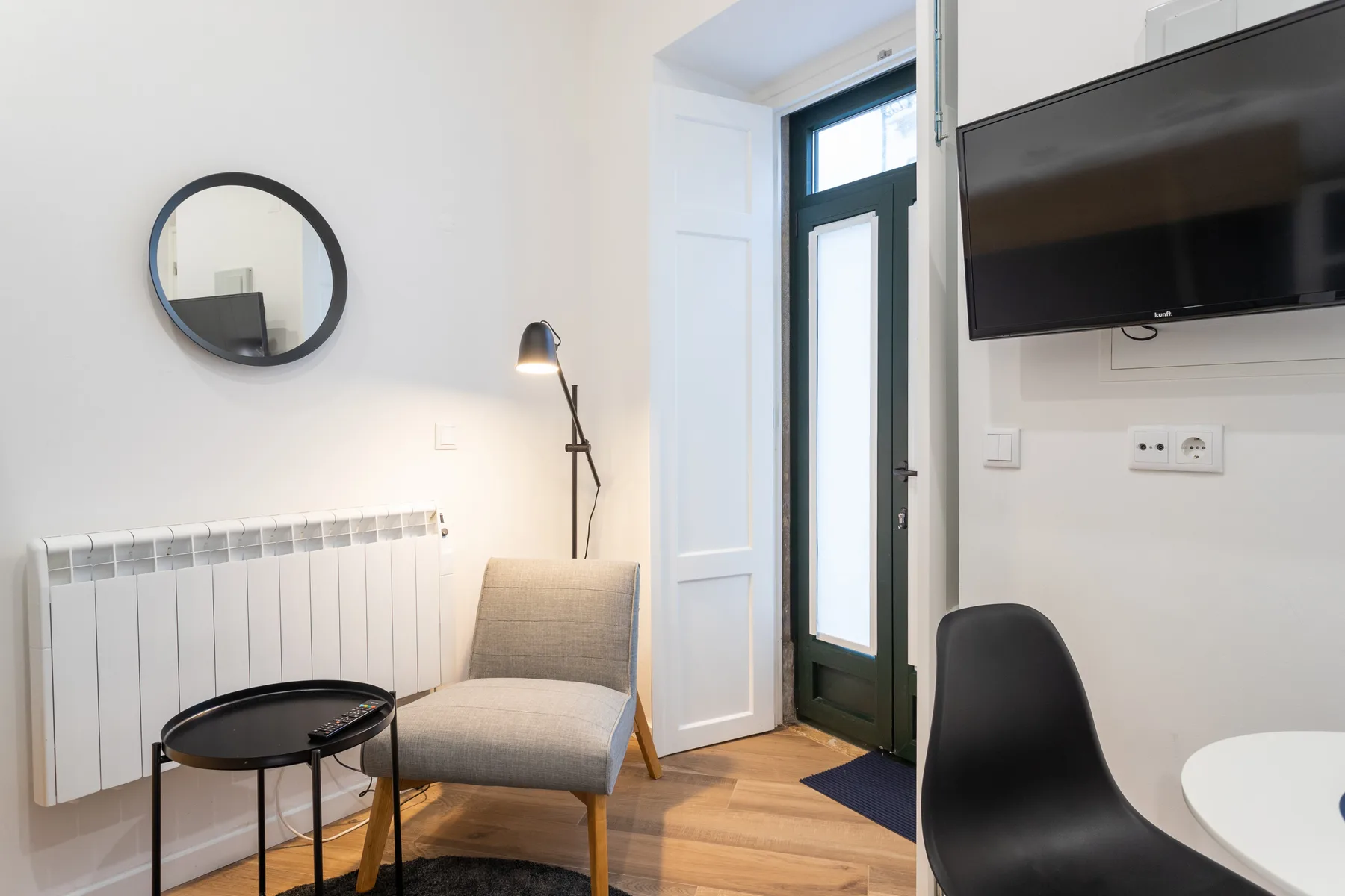 Una sala de estar luminosa con asientos, un televisor en la pared y una ventana alta.