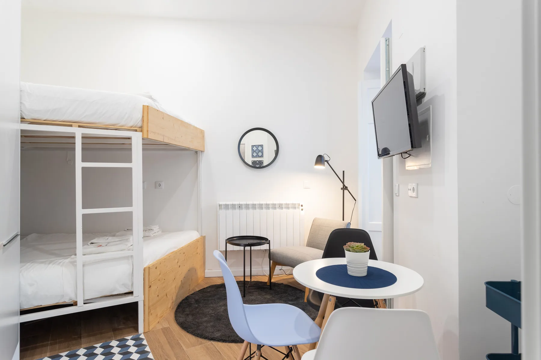 Un estudio luminoso con literas, una pequeña zona de estar y un televisor en la pared.