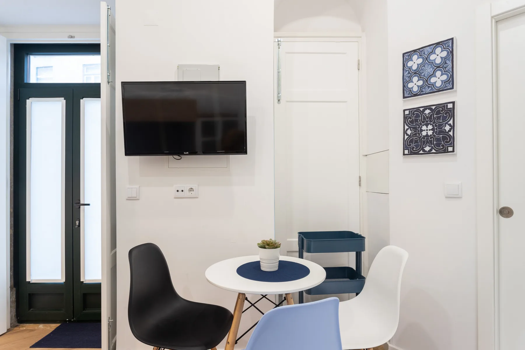 Un comedor luminoso con una mesa redonda, asientos y un televisor en la pared.
