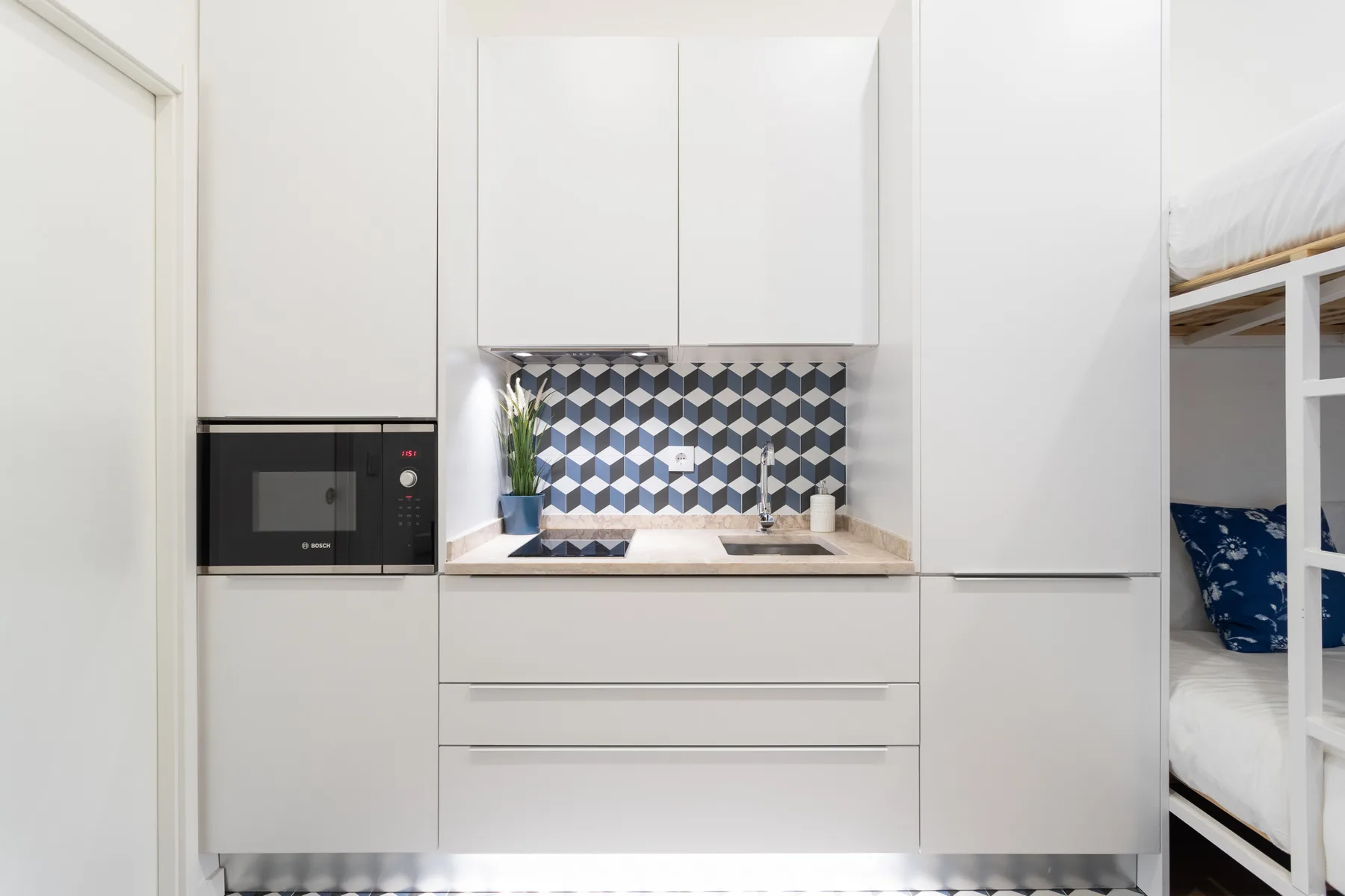 Una cocina compacta con armarios blancos, microondas integrado y salpicadero estampado.