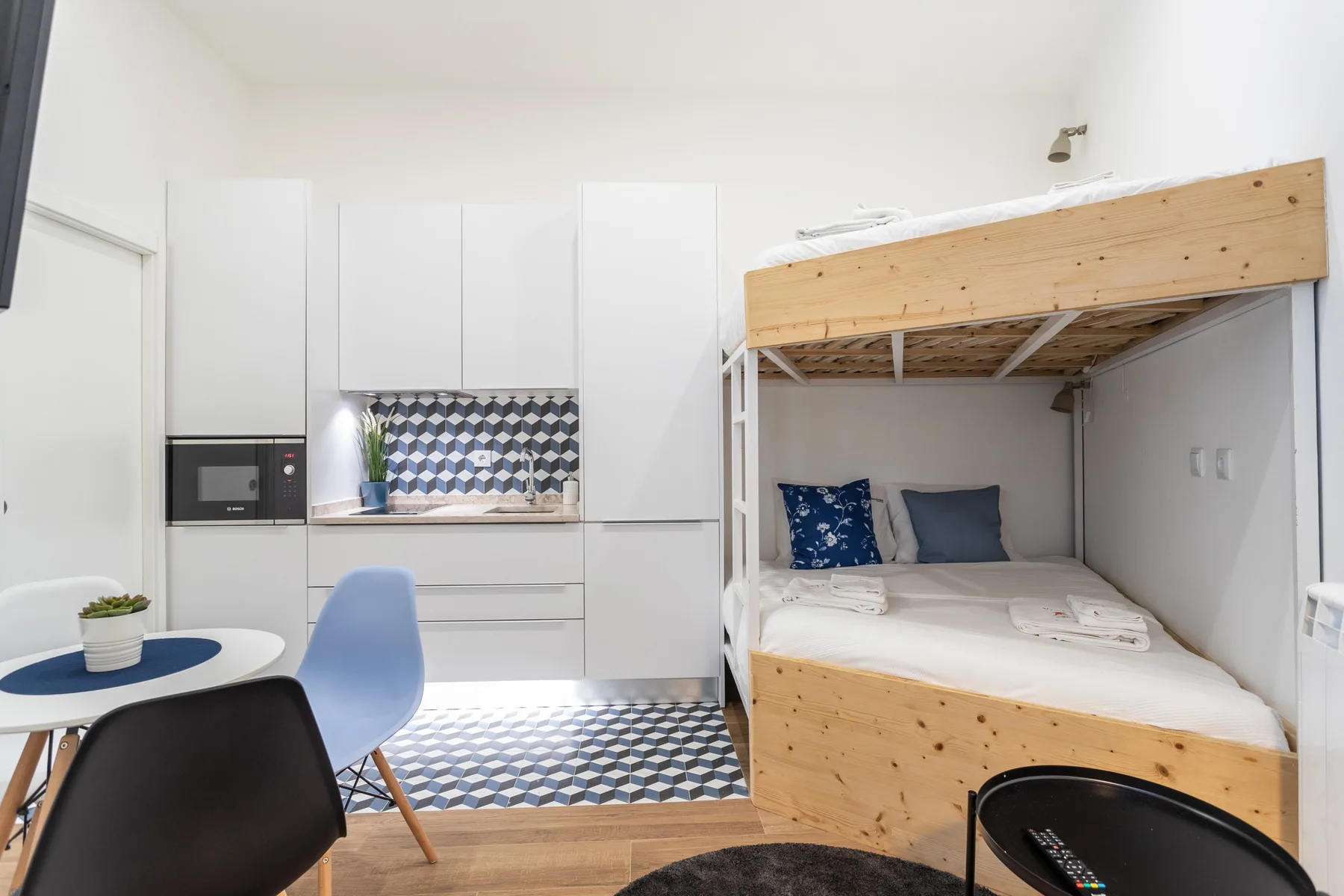 Un dormitorio compacto con cocina pequeña y una cama elevada sobre la zona de descanso.