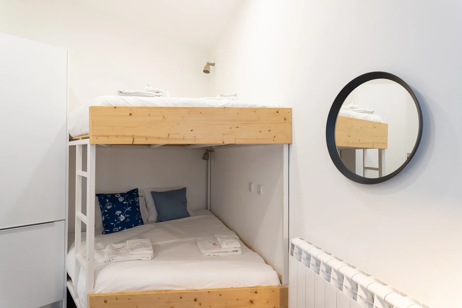 Un dormitorio compacto con una litera de madera y un espejo redondo en la pared.