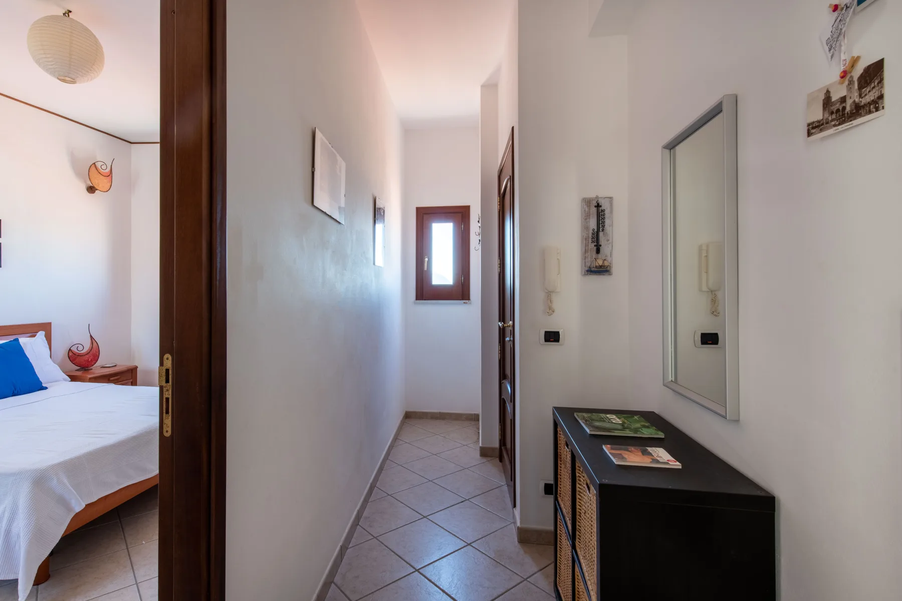 A narrow hallway leads past a bedroom, with a cabinet and mirror along the wall.