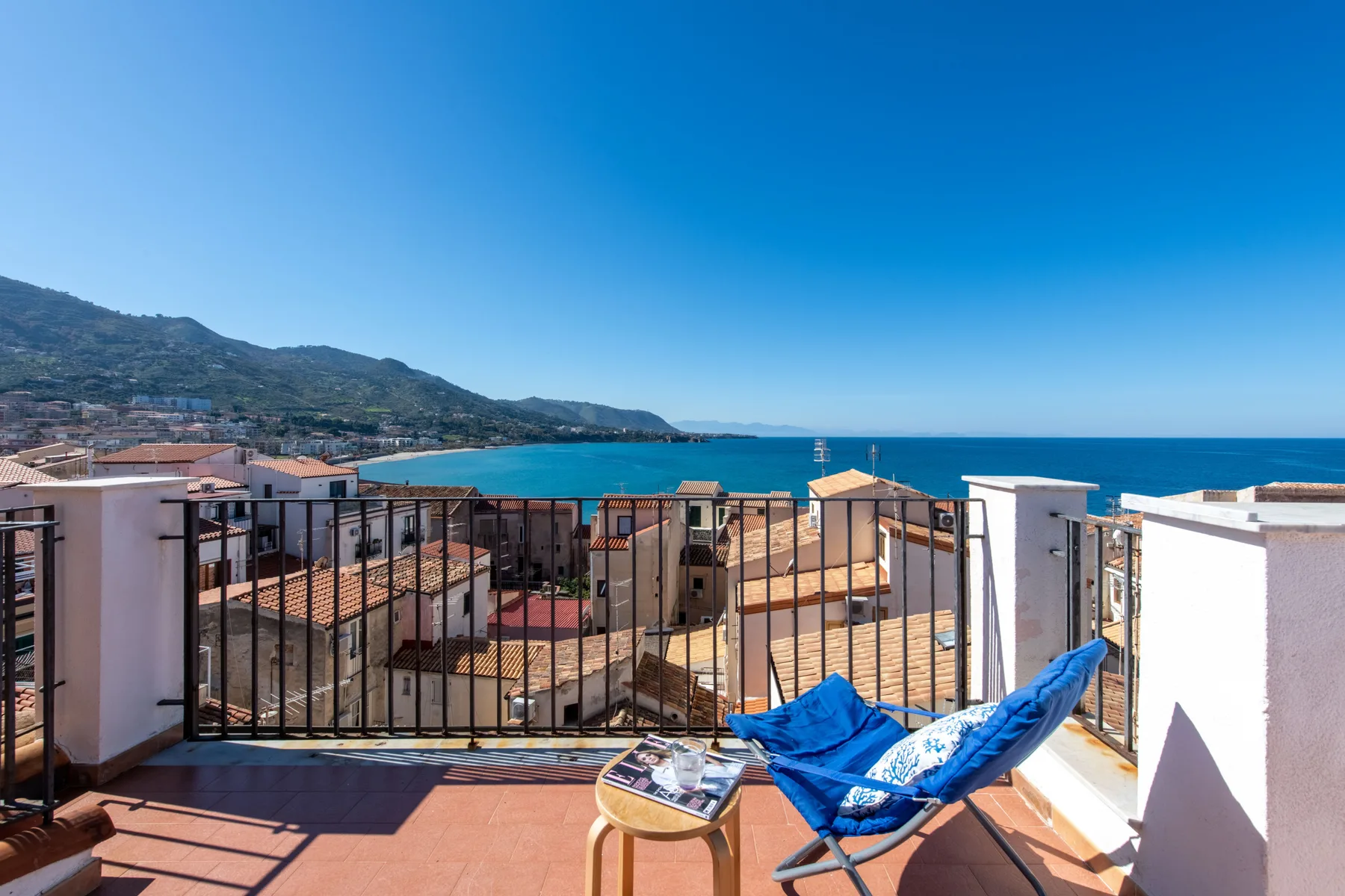 A rooftop terrace overlooks coastal buildings and the blue sea.