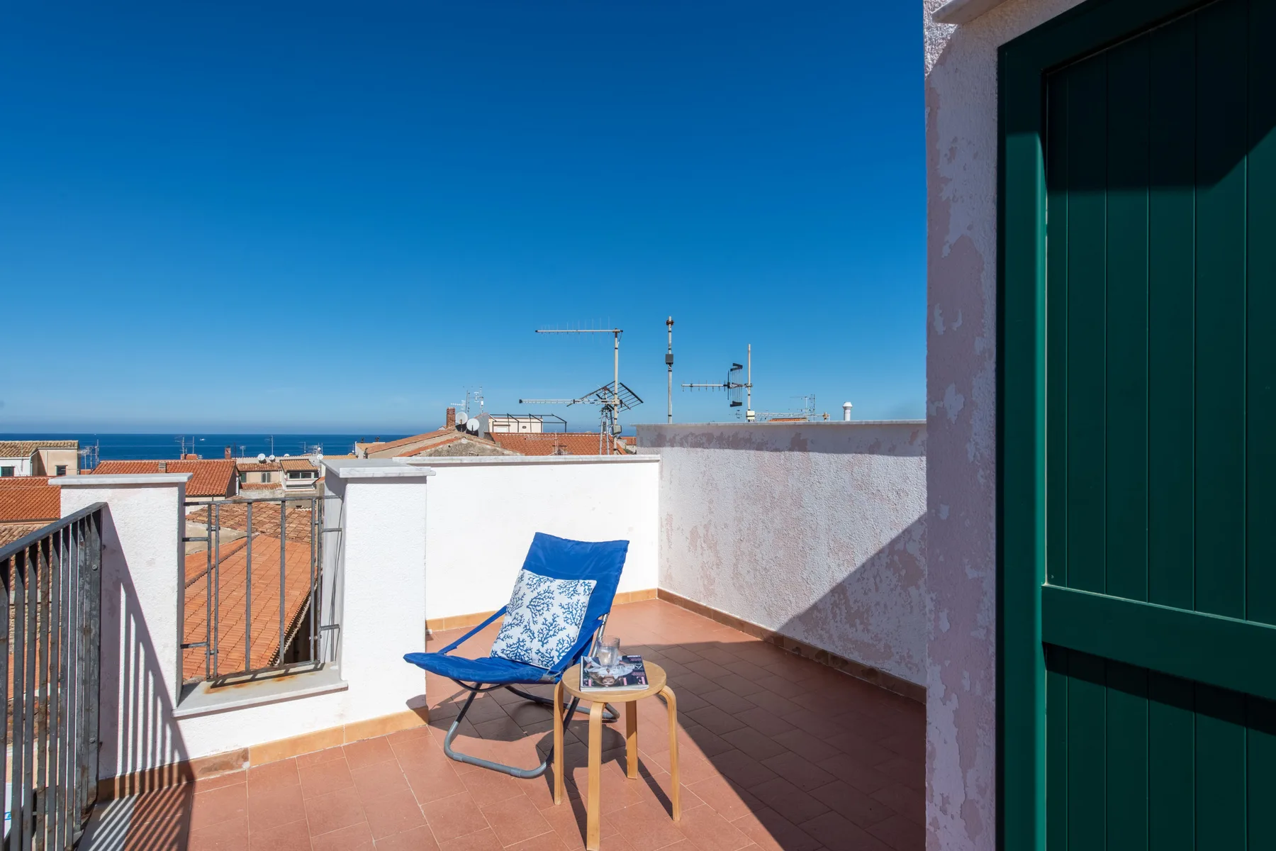 A sunlit rooftop terrace with blue seating and views of the sea.