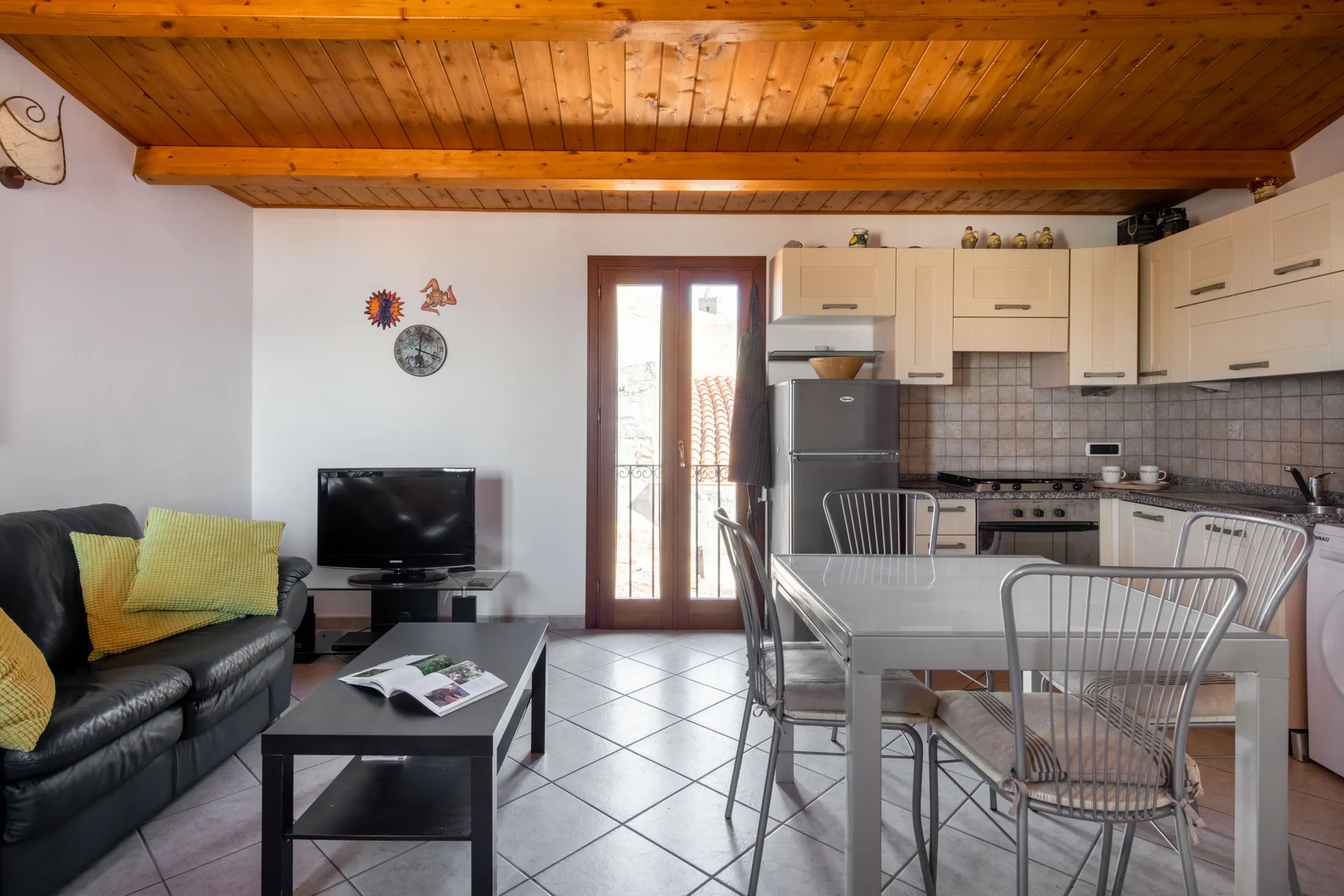 An open-plan living and kitchen area has a dining table and dark seating.