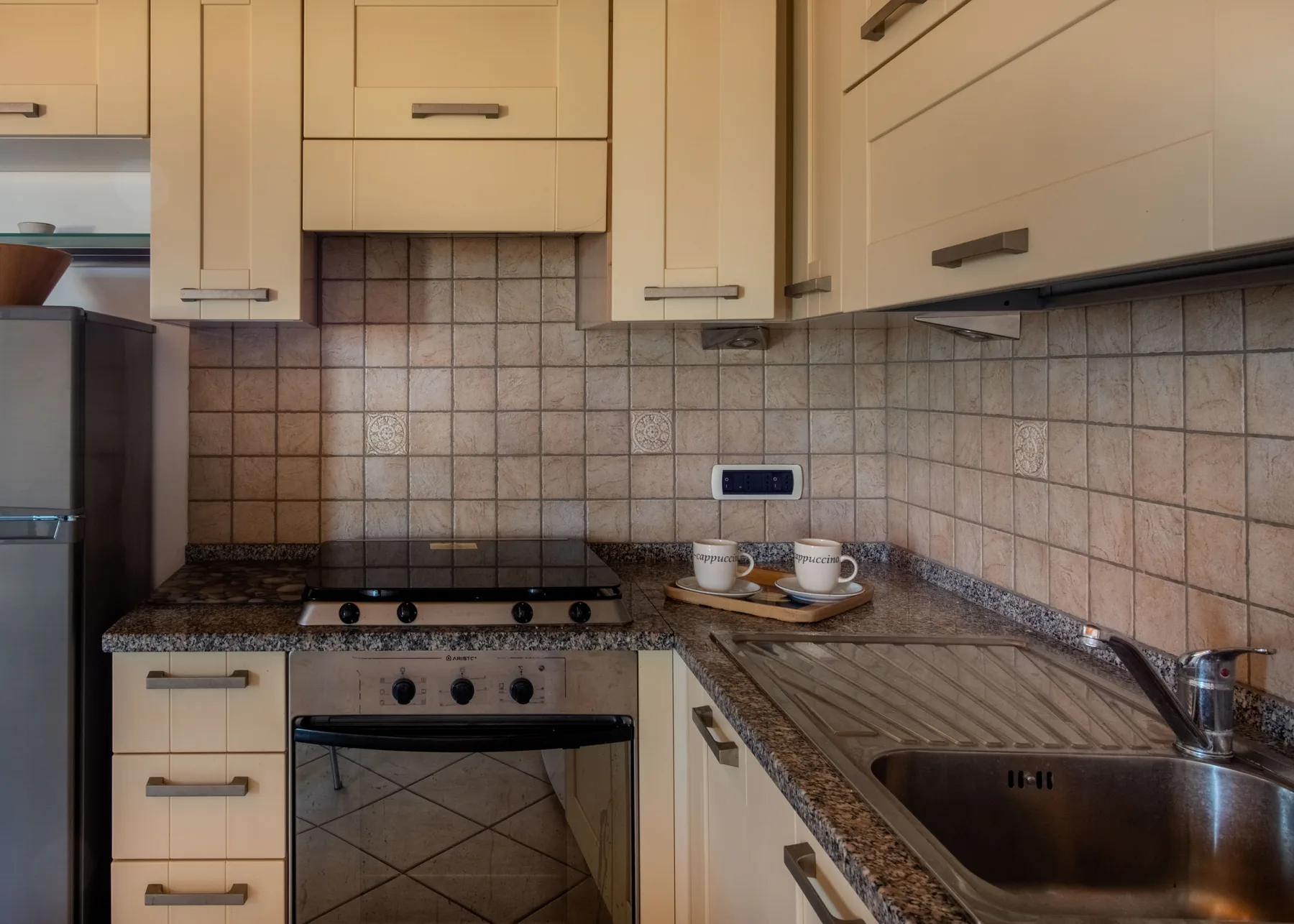 A compact kitchen with light cabinets, a tiled backsplash, and a countertop sink.