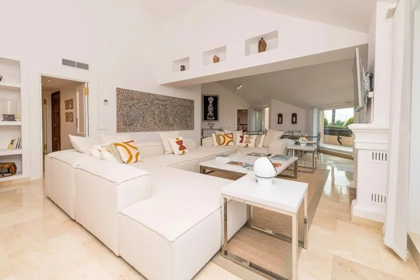 A bright living room with white seating and a glass dining area.