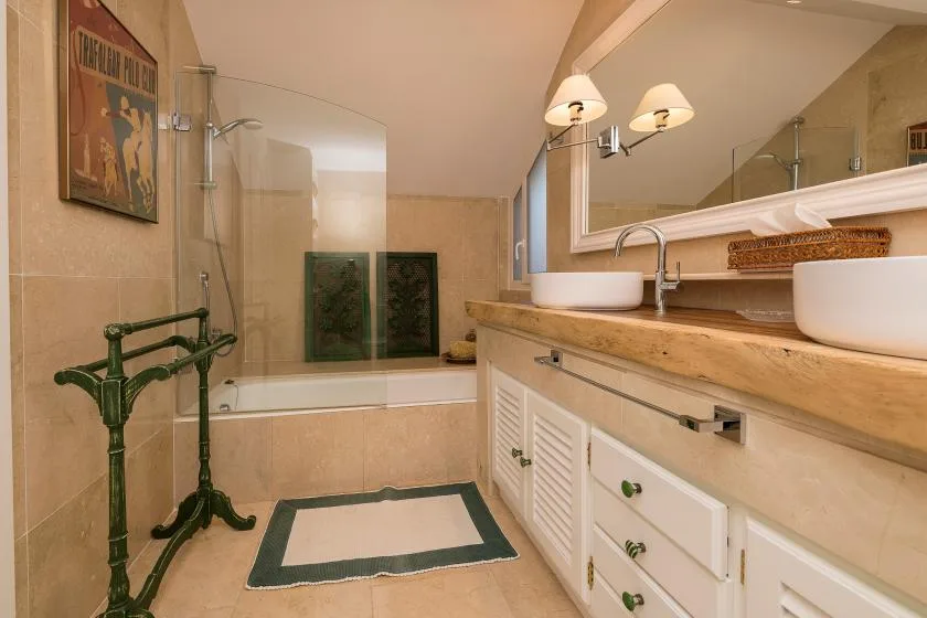 Un baño alicatado con bañera, mampara de ducha de vidrio y lavabo con mueble.