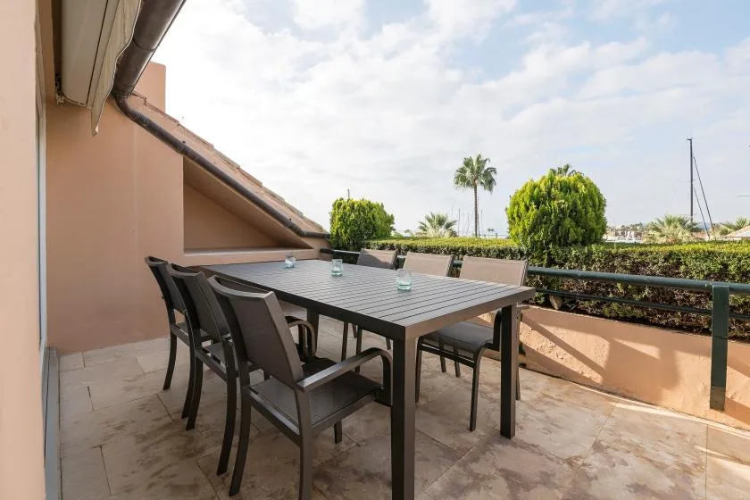 Una zona de comedor al aire libre con mesa y asientos en una terraza embaldosada.