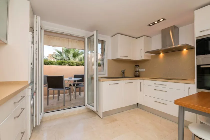 Una cocina luminosa con gabinetes blancos se abre a un pequeño comedor exterior.