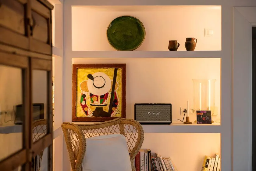 Una sala de estar cálidamente iluminada tiene estantes empotrados y una silla tejida.