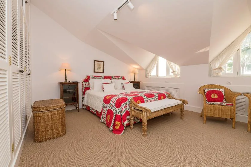 Un dormitorio abuhardillado luminoso con una cama cubierta por una colcha floral roja.