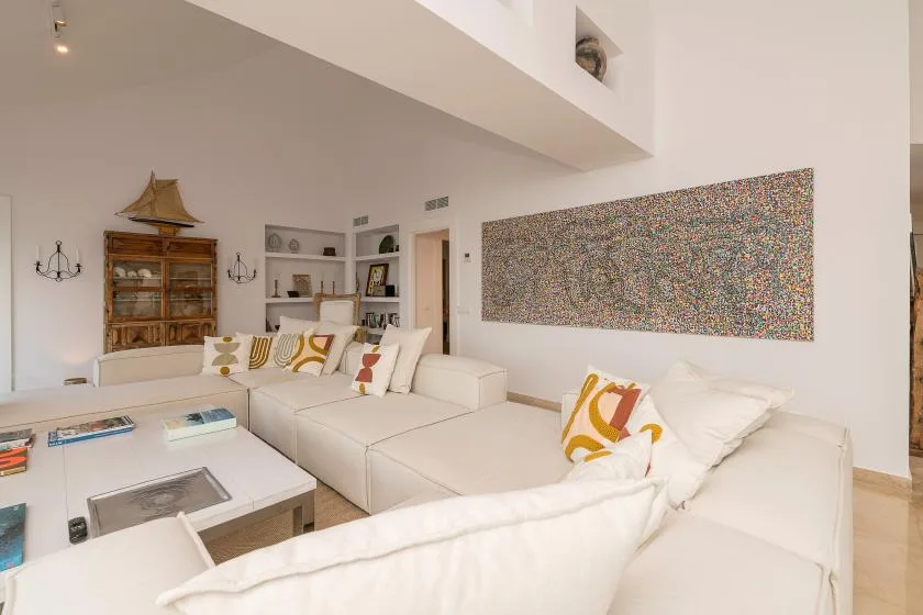 A bright living room with white seating and a large colorful abstract artwork.