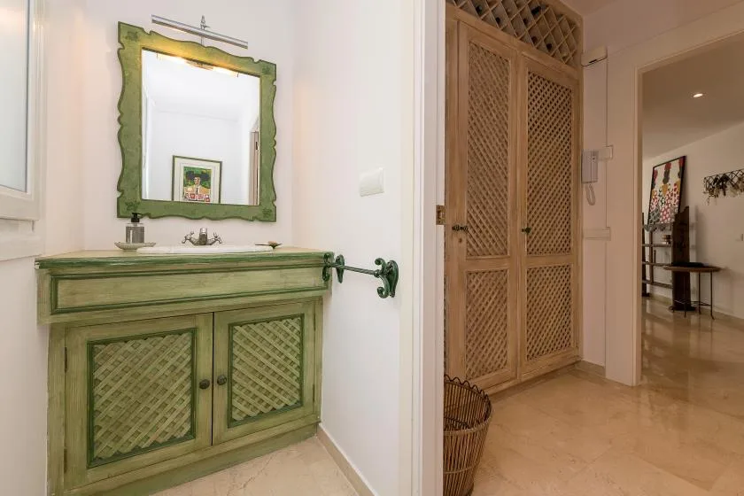Un mueble de baño con un espejo de marco verde está junto a un armario de celosía de madera.