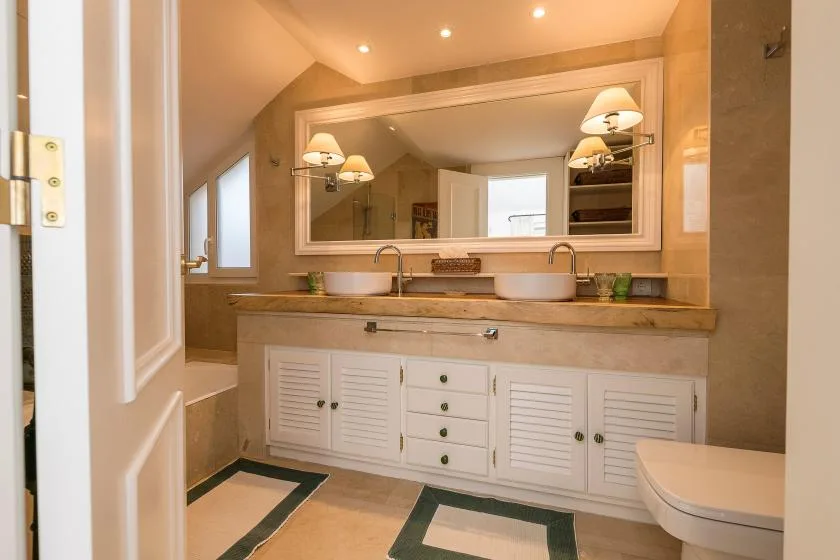 Un tocador de baño con dos lavabos está bajo un espejo grande.