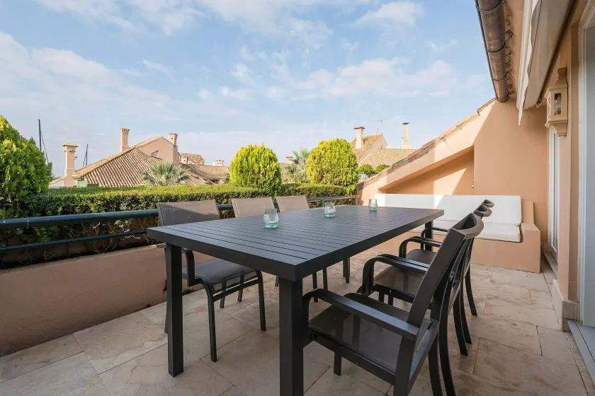 Una terraza en la azotea con una mesa de comedor y asientos junto a un muro bajo.
