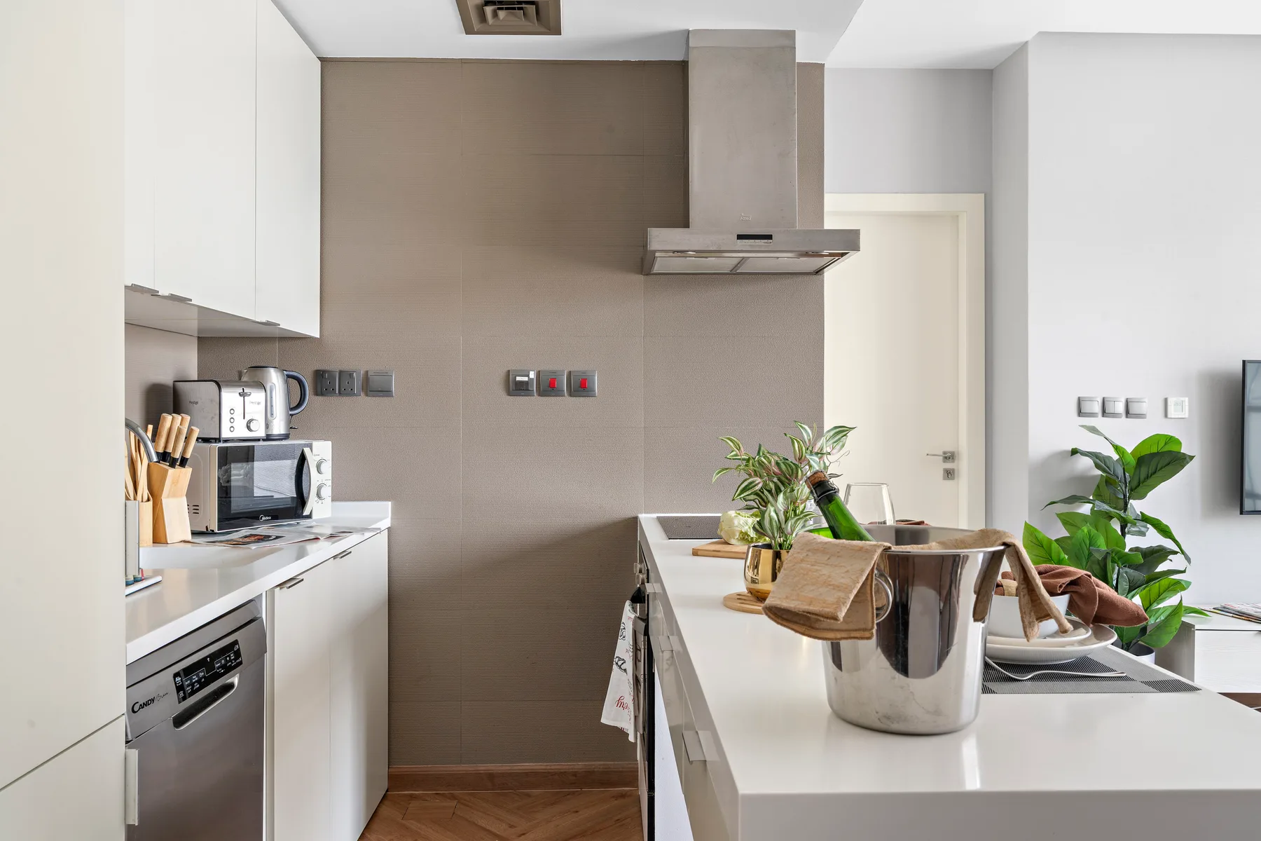 A modern kitchen with a central island, countertop appliances, and potted plants.