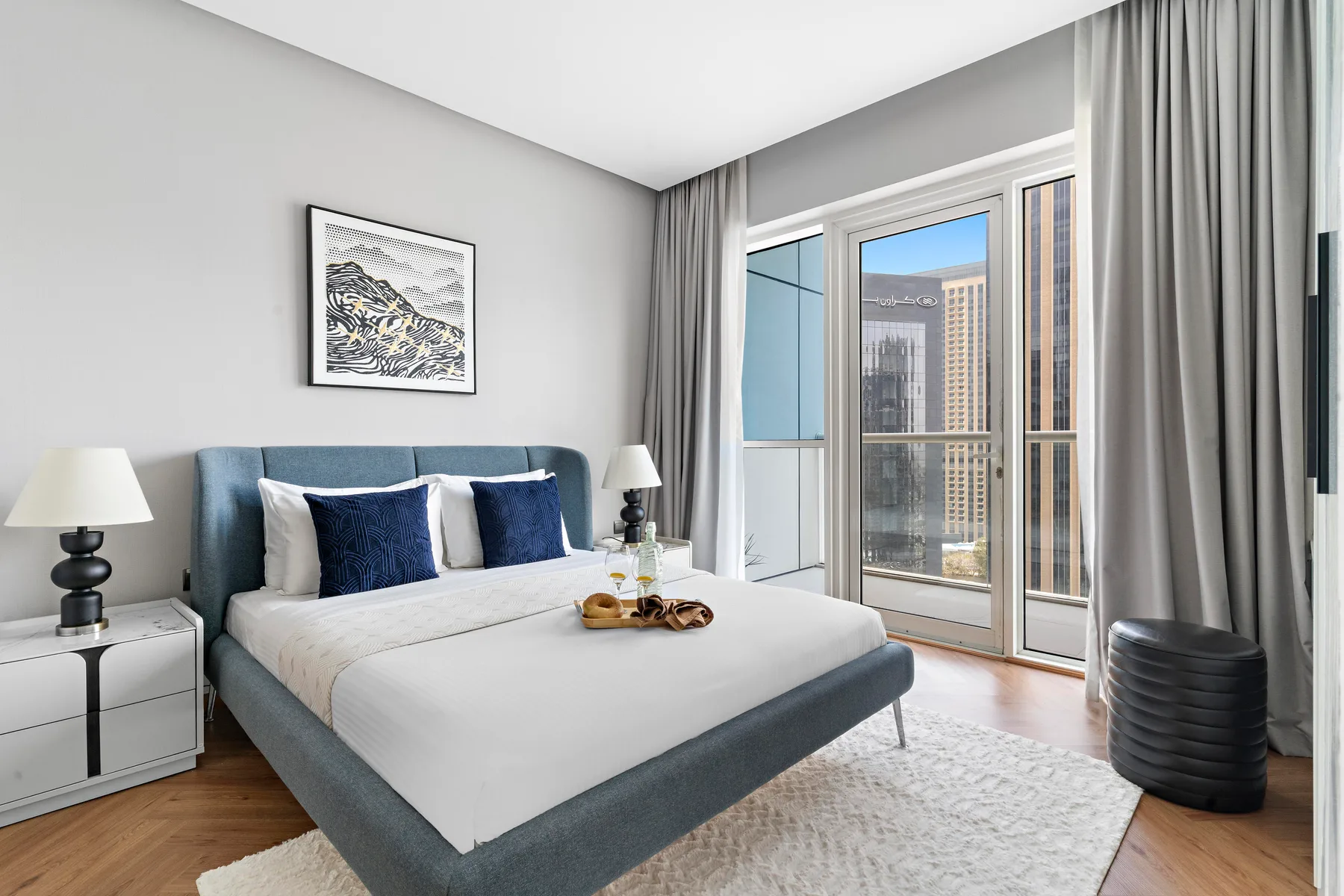 A bright bedroom with a bed, bedside tables, and tall windows.