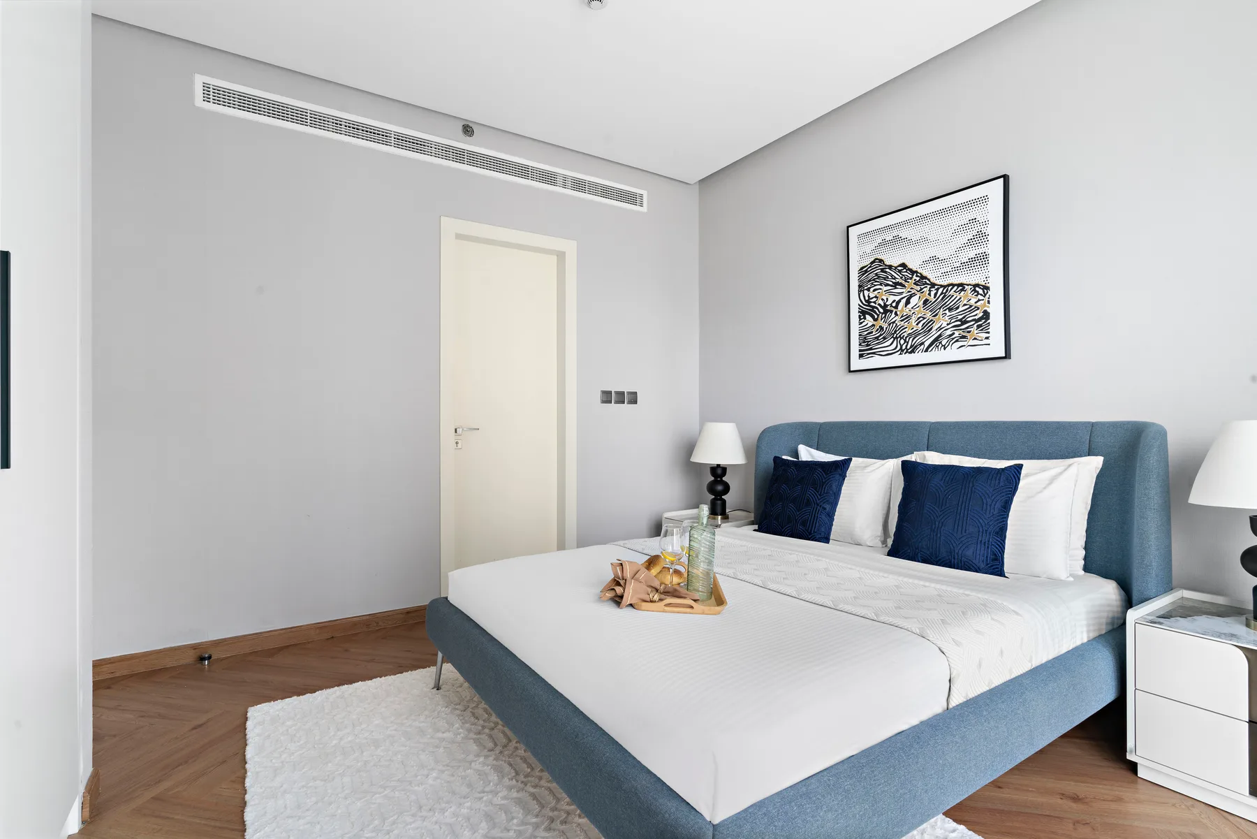 A bright bedroom with a blue upholstered bed and framed artwork above it.