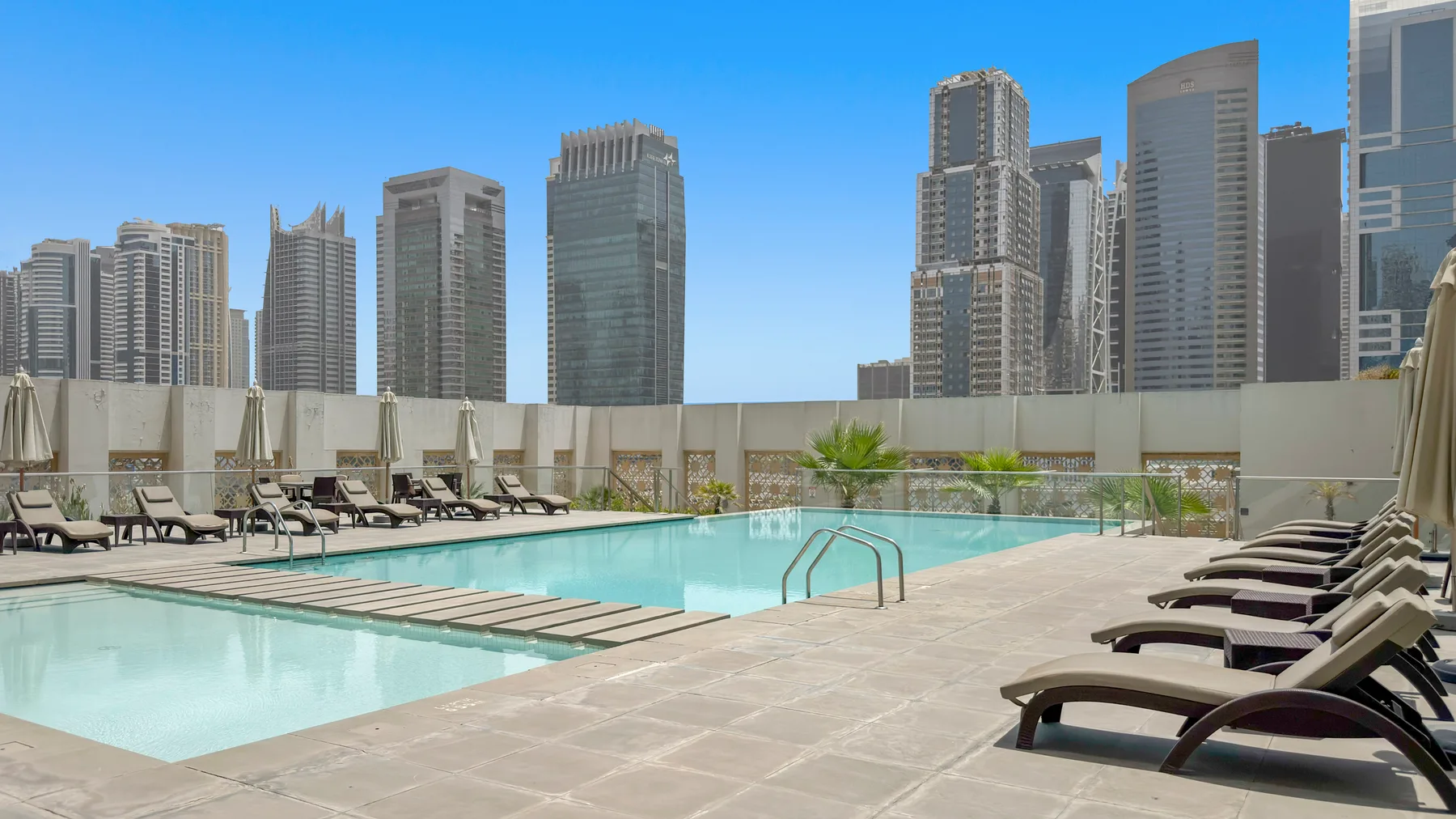 A rooftop swimming pool is surrounded by lounge seating, with city buildings in the background.