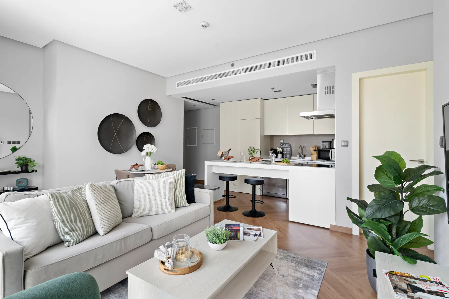 A bright living room opens onto a white kitchen, with seating around a coffee table.